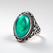 Color-changing mood ring with ornate filigree band and teal thermochromic stone — white background